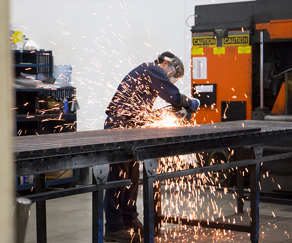 Operations associate using a grinder on a Bar Grating panel.