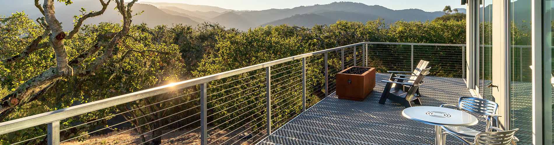 Hero image of a balcony with flooring made out of bar grating, overlooking trees and mountains.